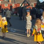 Barn i folkdräkt gåendes mot en midsommarstångsresning.