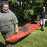 En kvinna och man som bär en kanot över en gräsmatta