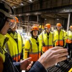 Kvinnor i varselkläder lyssnar på en man som berättar något.